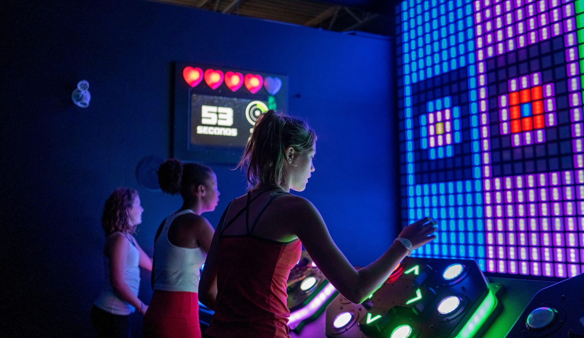 Three girls playing an arcade-style game with a light-up screen.